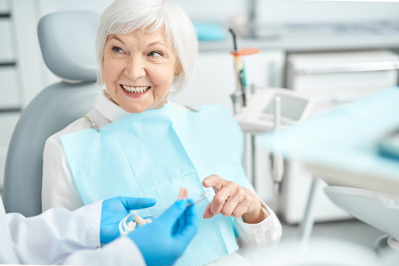 An image of an older woman sitting in a dental chair after a dental implant procedure